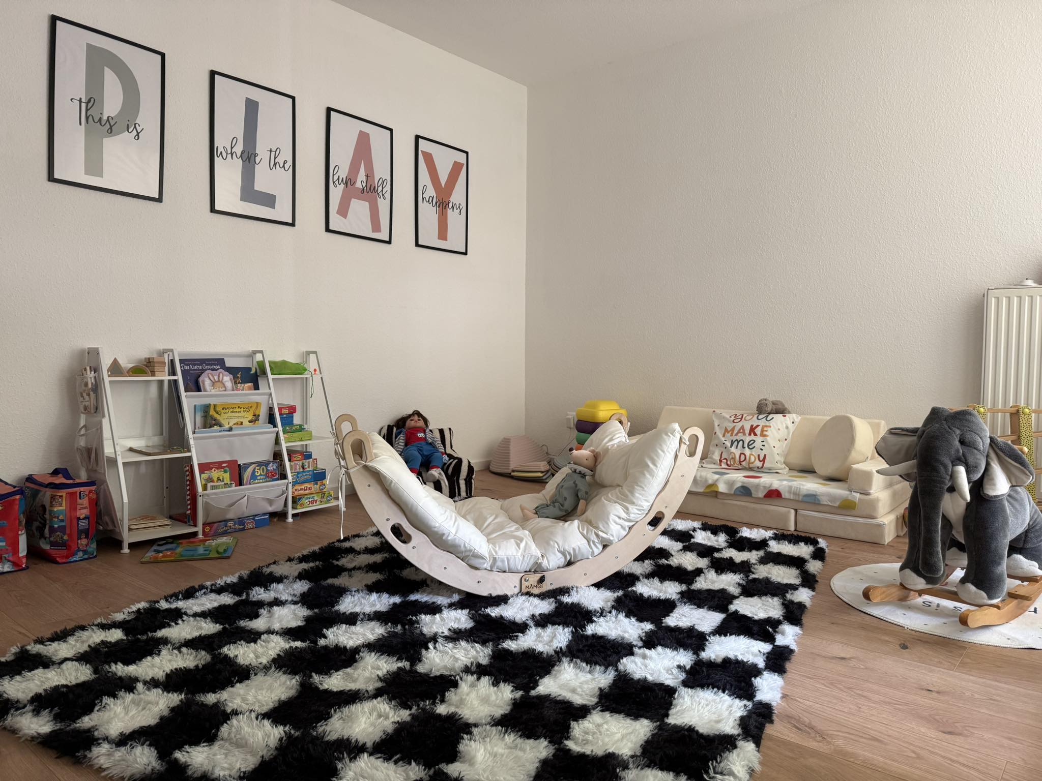 Der helle Hauptspielbereich der Kindertagespflege Kinder(t)raum in Weinheim mit PLAY-Wandbildern, Mamoi-Schaukel und Kuschelecke