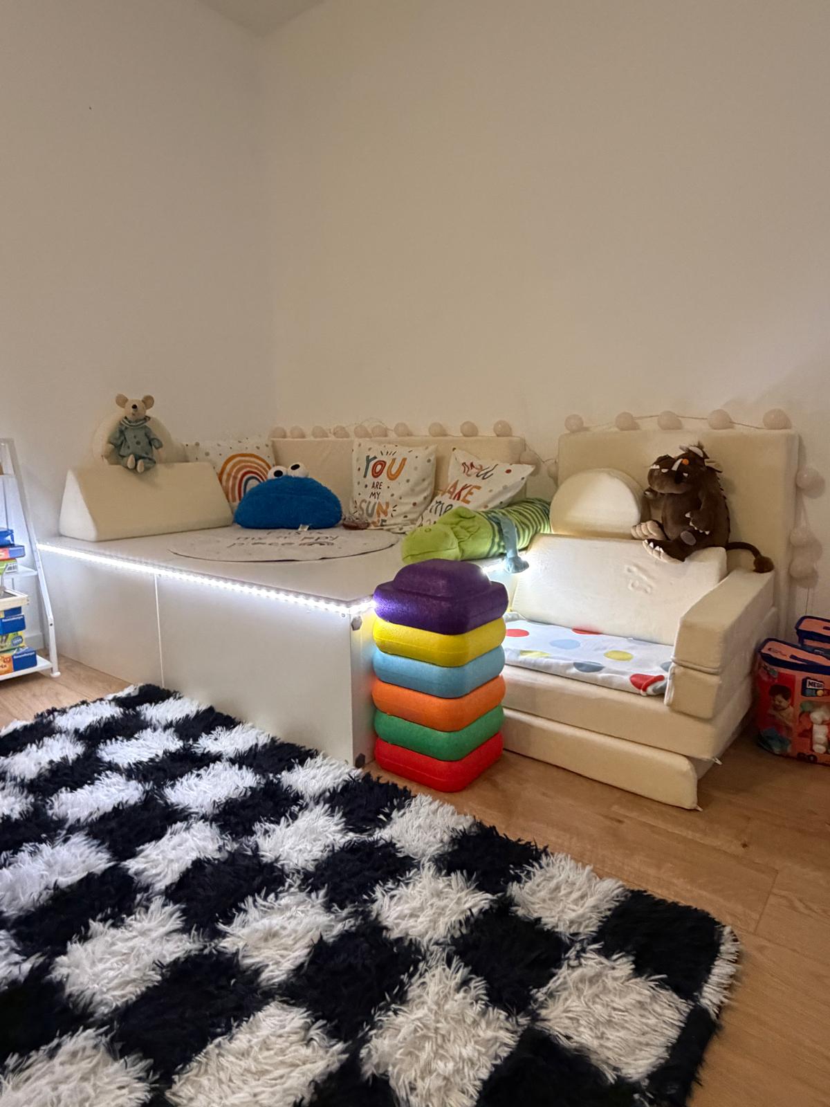 Gemütliche Sofaecke mit weicher cremefarbener Couch, Kissen, Kuscheltieren und bunten Schaumstoff-Bausteinen